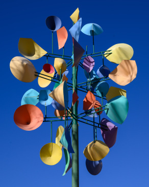 A multicolor wind scuplture spins in the air against a bright blue sky in downtown Denver, Colorado.