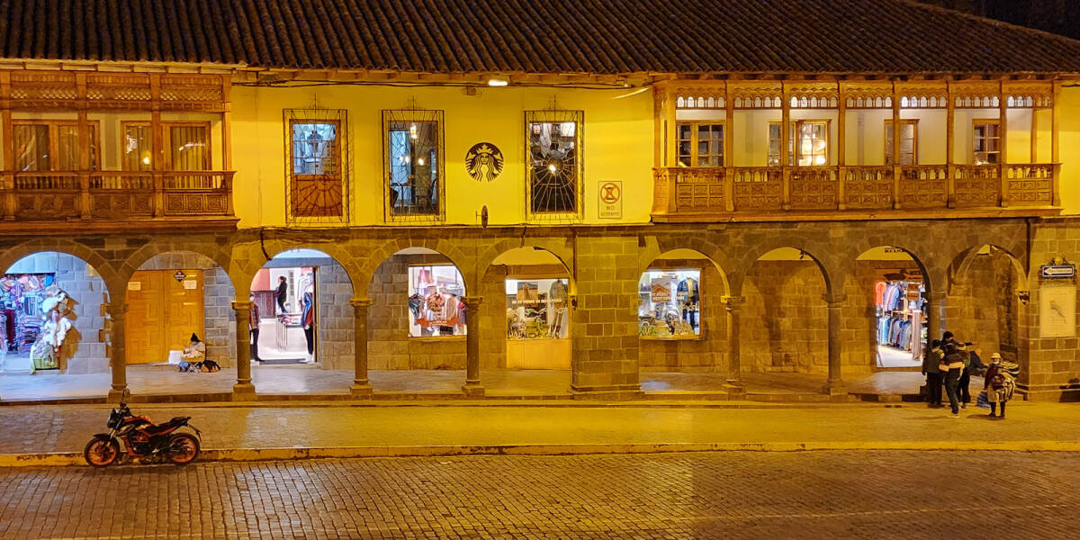 Section of shops lining the side of Plaza de Armas in Cusco glows in the golden street light.