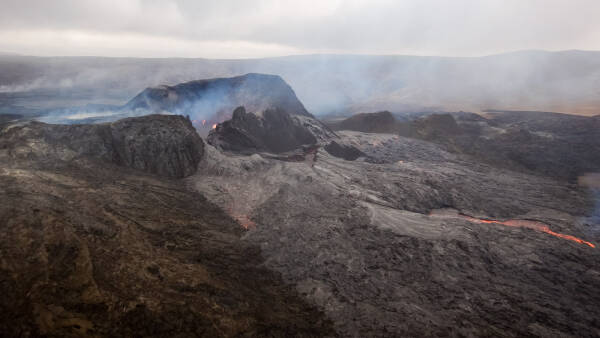 Lava flows and smoke rises around the top crater of the Fagradalsfjall volcano in Iceland.