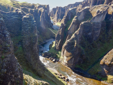 A river of brown and blue flows between the cliffs of Fjadrargljufur canyon in Iceland.