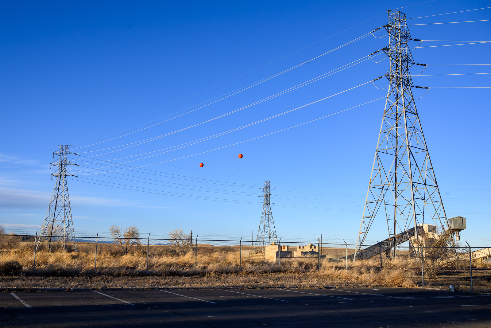 Electrical transmission towers balance a pair of orange balls between them in front of Valmont Power Station in Boulder, Colorado.
