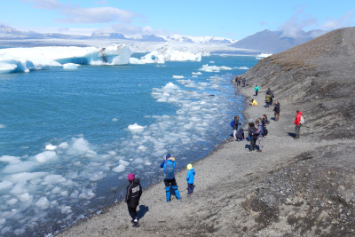 Colorfully dressed tourists line the shore of the Jokulsarlon glacier bay in Iceland.