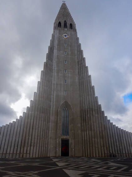 Thin stone columns rise into a cloudy Reykjavik sky around the main tower of HallgrÃ­mskirkja.