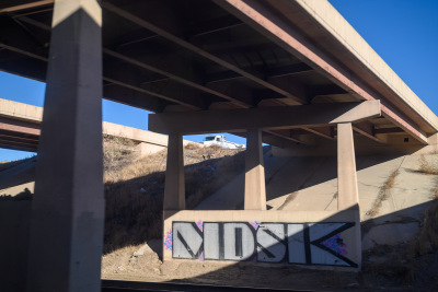 Blocky graffiti decorates a highway overpass seen from an RTD Green Line train near Denver, Colorado.
