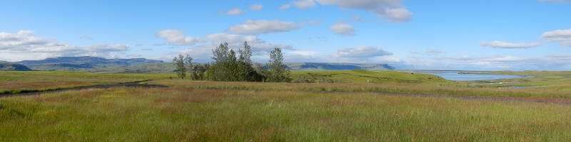 Panoramic view of green grass fields with distant mountains and lakes in Iceland near the village of Kirkjubaejarklaustur