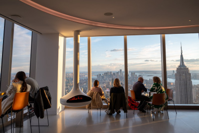 People watching the view at One Vanderbilt in New York City around a futuristic fireplace.