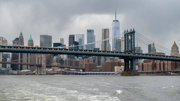 Lower Manhattan rises behind the Manhattan Bridge on a rainy day from a boat on the East River in New York.