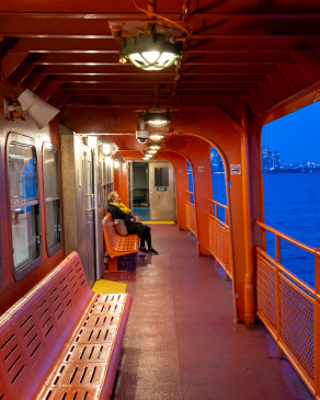 Women sits alone on the Staten Island Ferry at dusk.