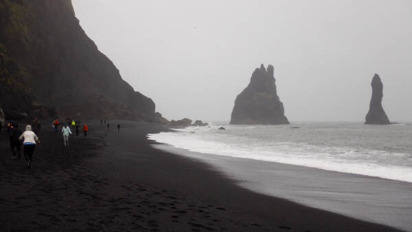 People in bright jackets are the only colors visible on a dark rainy day at Reynisfjara black sand beach in Iceland.