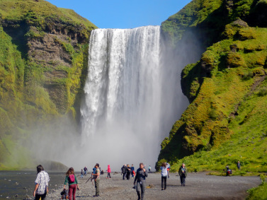 People stand in front of the huge SkÃ³gafoss waterfall in Iceland.