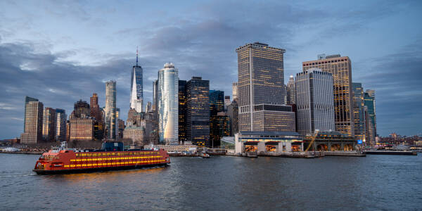 Orange Staten Island Ferry boat approaches the dock in Lower Manhattan on a cloudy evening before sunset.