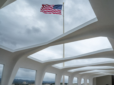 US flag flies above the USS Arizona Memorial at Pearl Harbor, Hawaii on a cloudy day.