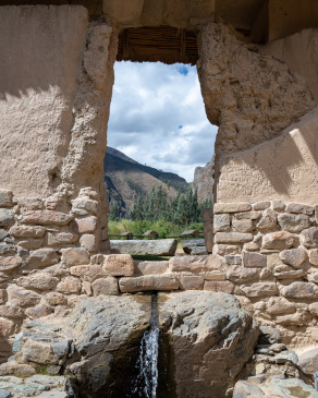 Main fountain at Ollantaytambo with a view of mountains through a window.