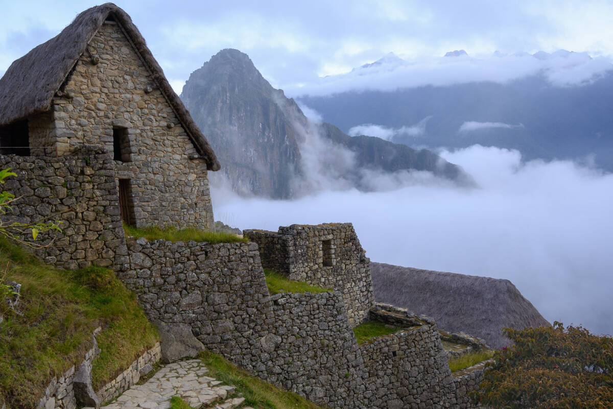 Huayna Picchu rises above the morning fog behind the first structures encountered at Machu Picchu.