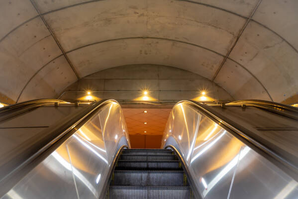 Three lights resemble angelic figures at the top of a metro station escalator.