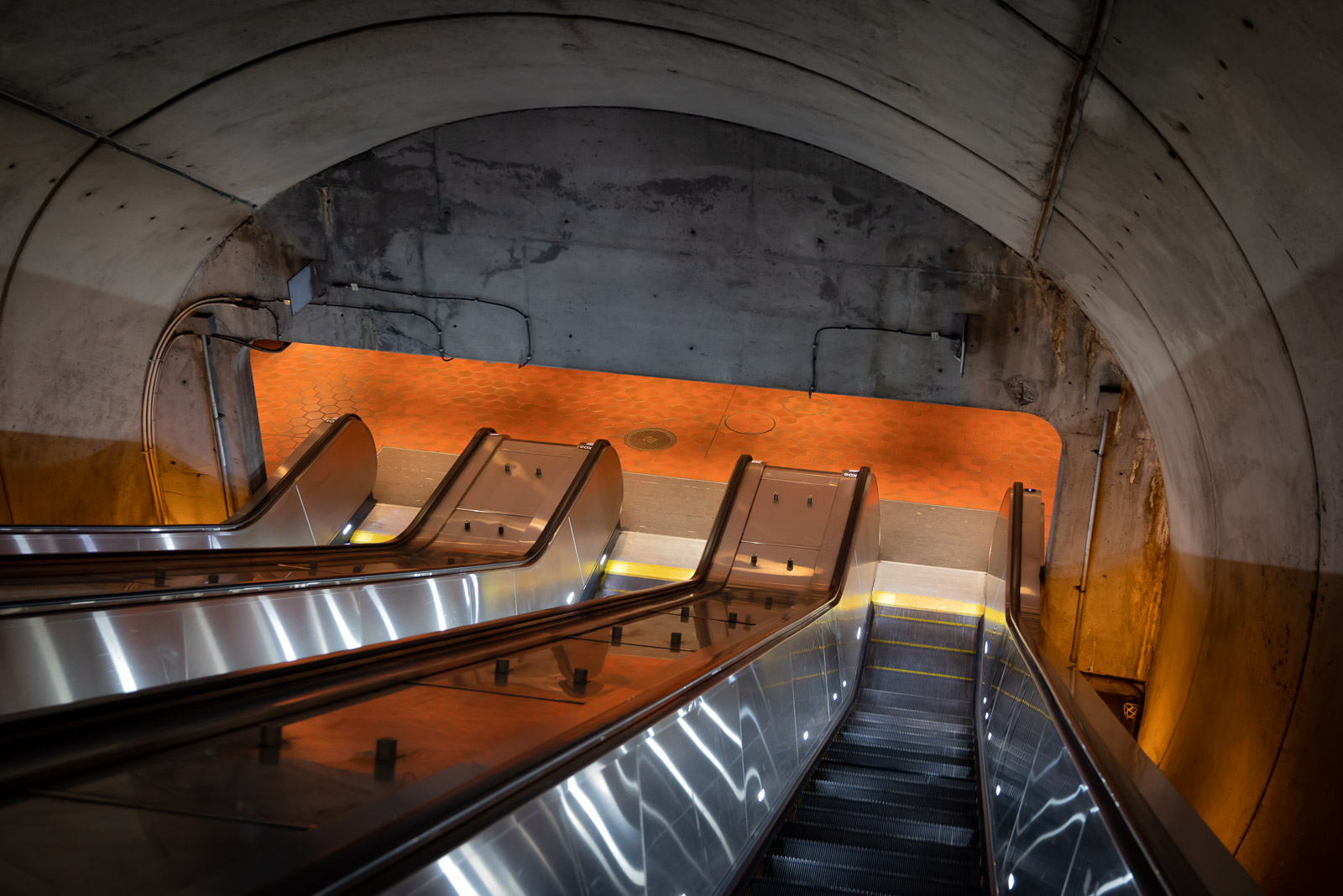 An ominous orange glow awaits at the dark end of a descending escalator.