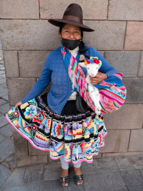 Woman in traditional Peruvian dress poses in front of stone wall.