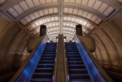 Blue lights illuminate twin escalators bridging levels at a DC Metro station.