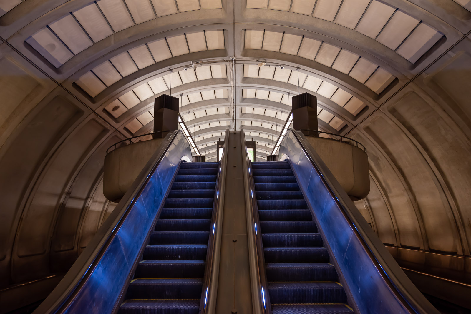 Blue lights illuminate twin escalators bridging levels at a DC Metro station.