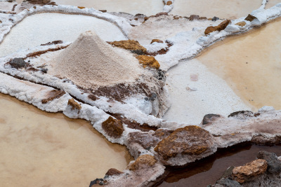 Pink Peruvian salt is piled next to an evaporation pool at Marasal salt mine in Maras, Peru.
