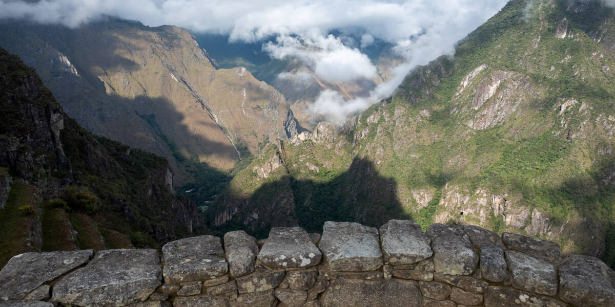 The shadow of Machu Picchu falls on the valley below a curving stone wall.