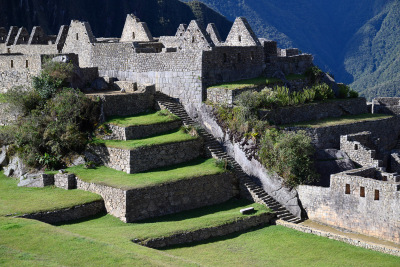 A dense area of stone buildings sits on top of a green terraced corner at Machu Picchu.