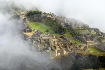The lush green central plaza of Machu Picchu emerges from the morning fog.