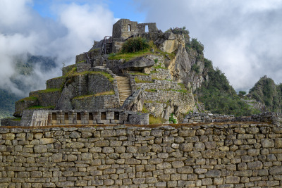 The mound where Intihuatana sits rises behind a stone wall at Machu Picchu.